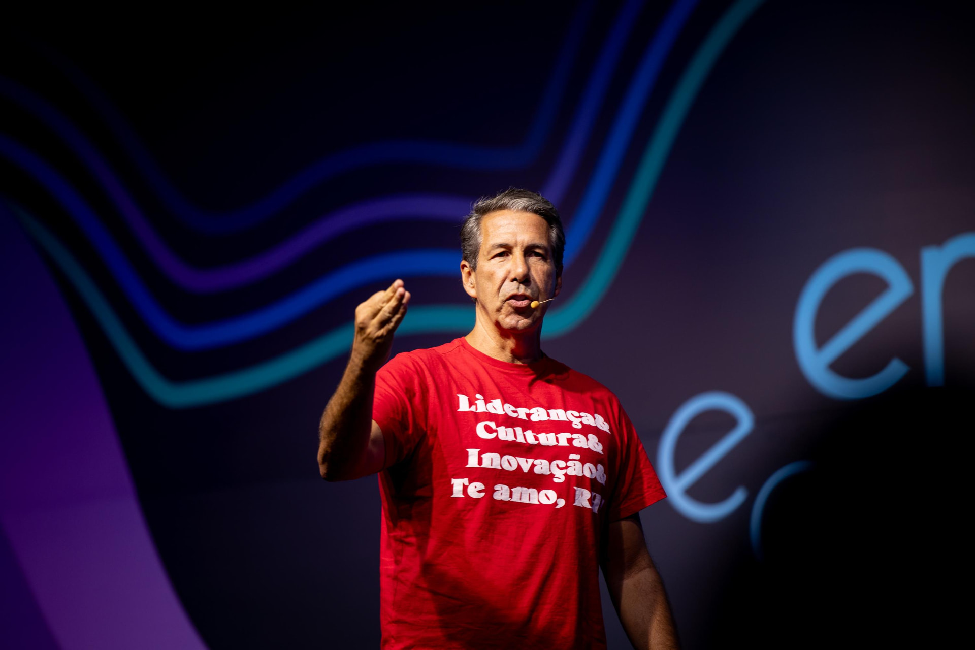 Adriano Lima de camiseta vermelha “Liderança, Cultura, Inovação — Te amo, RH!” gesticulando no palco